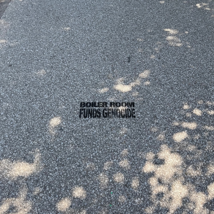 Graffiti on asphalt reading “Boiler Room Funds Genocide”.