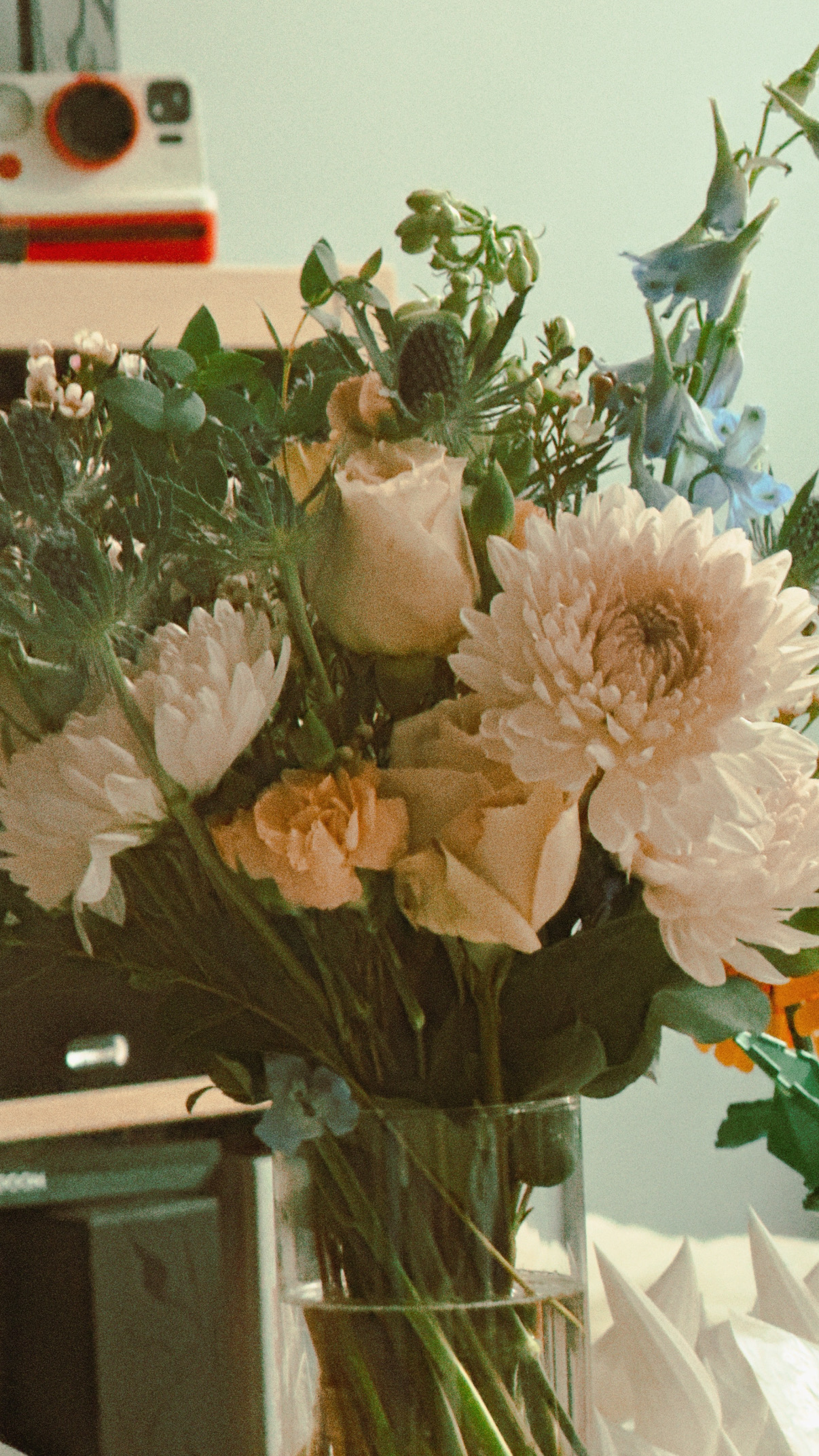 A bouquet of pale roses and white chrysanthemum-like blooms in a glass vase, shot indoors with a soft film-like grain.