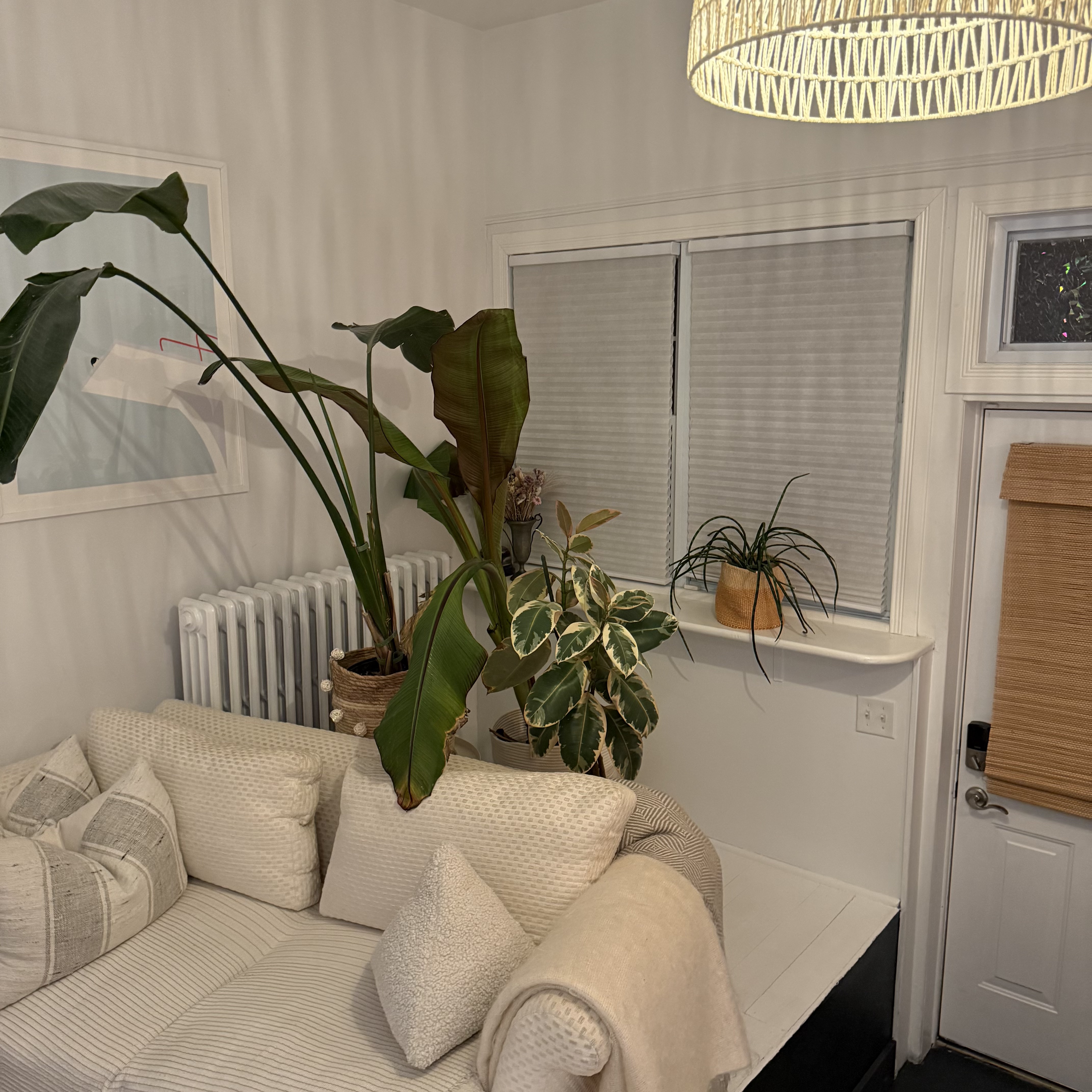 A small dining nook with a rattan pendant light, pink tulips in a glass vase, and a vintage pull-down world map on the wall.
