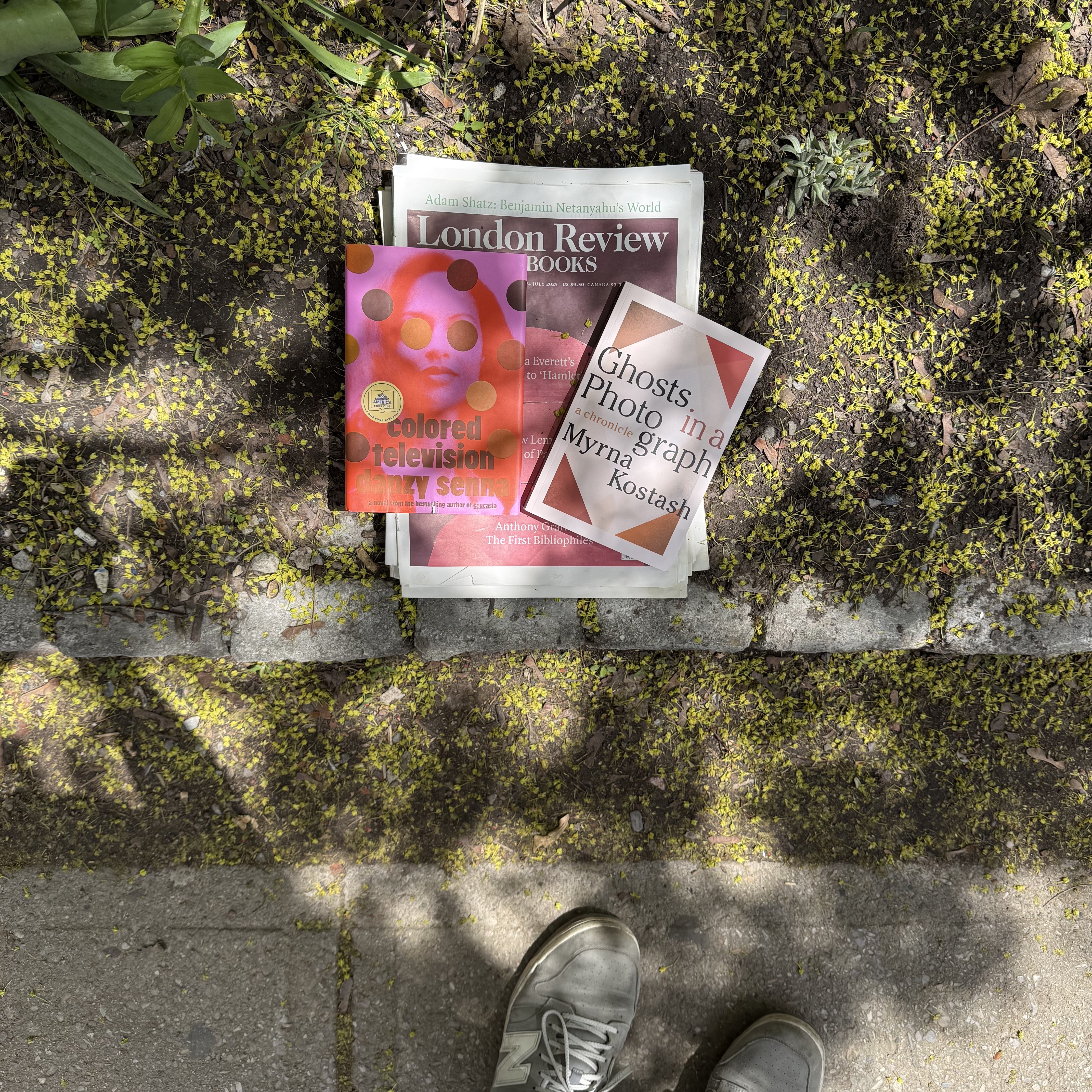 Two boooks,Colored Television by Danzy Senna and Ghosts Photo in a graph a chronicle by Myrna Kostash, sitting on a stack of London Review of Books.
